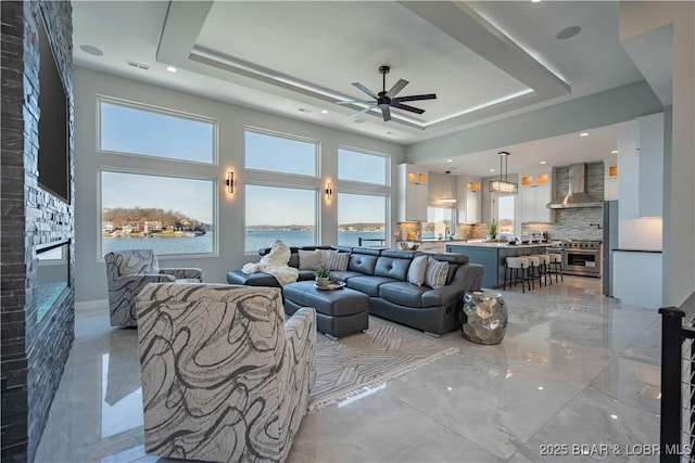 living room featuring a water view, ceiling fan, and a raised ceiling