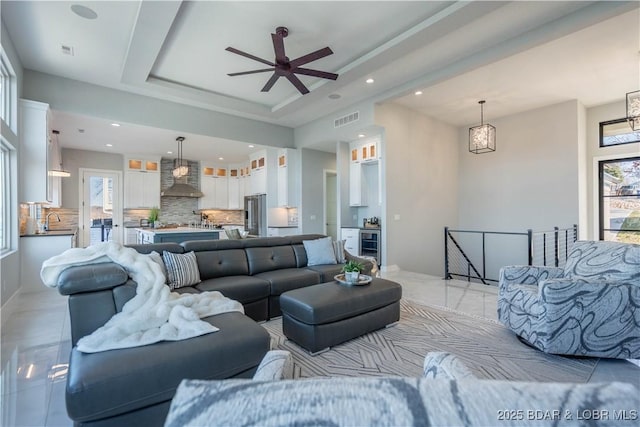 tiled living room with ceiling fan with notable chandelier, sink, beverage cooler, and a raised ceiling