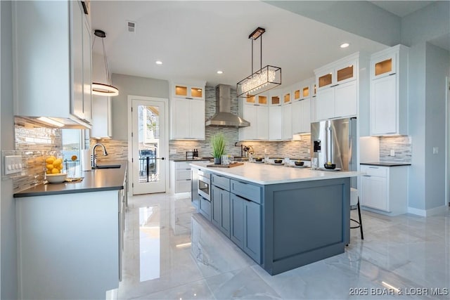 kitchen with a large island, stainless steel appliances, pendant lighting, wall chimney exhaust hood, and white cabinets