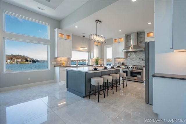 kitchen with appliances with stainless steel finishes, wall chimney range hood, white cabinetry, and pendant lighting