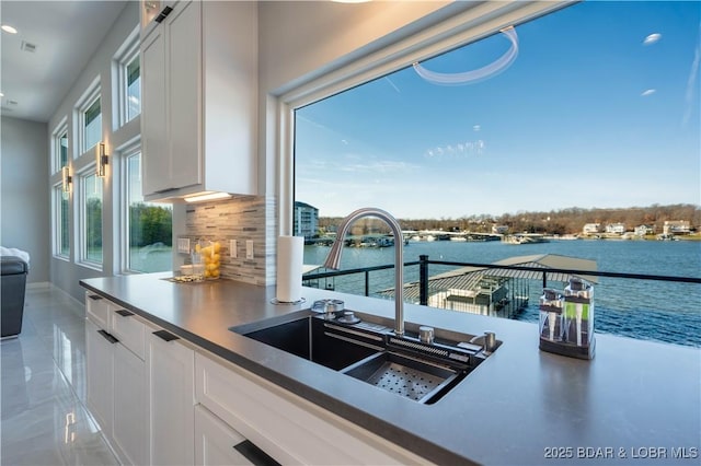 kitchen featuring sink, white cabinets, a water view, and a healthy amount of sunlight