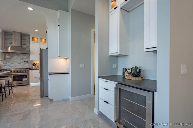 kitchen with white cabinets, wall chimney exhaust hood, stainless steel appliances, wine cooler, and decorative backsplash