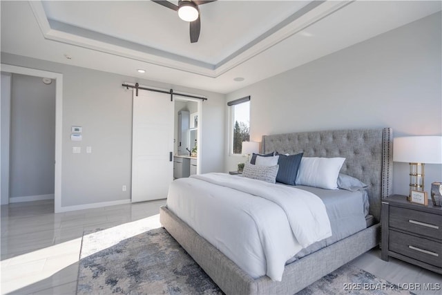 bedroom featuring ceiling fan, a barn door, a tray ceiling, and ensuite bathroom