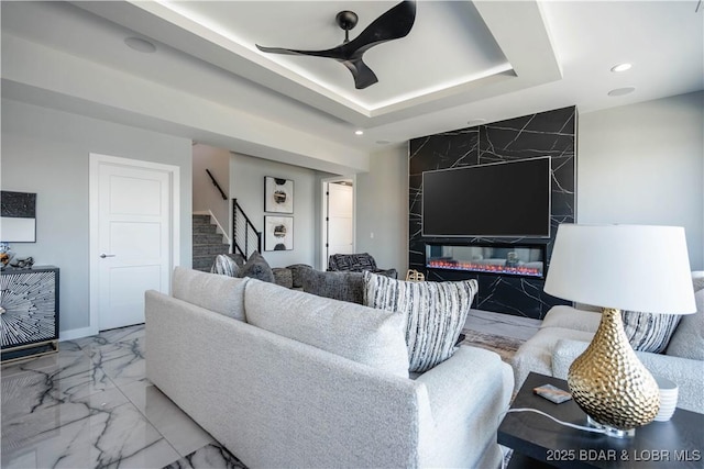 living room with ceiling fan, a tray ceiling, and a premium fireplace