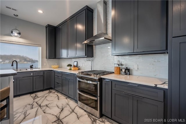 kitchen featuring decorative light fixtures, wall chimney range hood, decorative backsplash, double oven range, and light stone counters