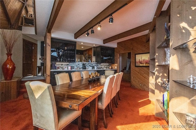 dining room featuring beamed ceiling, wood walls, carpet floors, and bar area