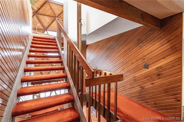 stairway with wooden ceiling, beam ceiling, and wooden walls