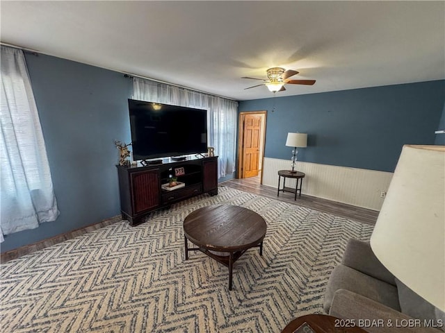 living room with a wainscoted wall and ceiling fan