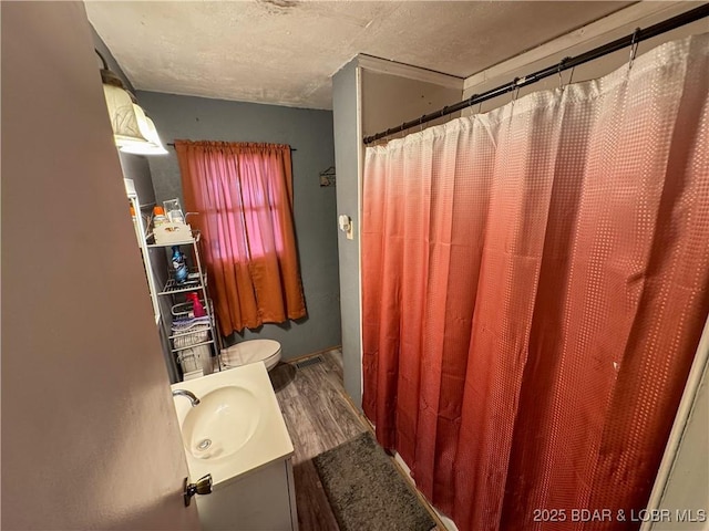 bathroom featuring a textured ceiling, toilet, wood finished floors, and vanity