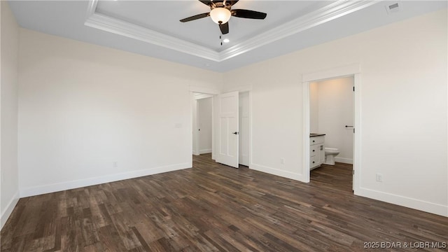 unfurnished bedroom with ensuite bathroom, ceiling fan, dark hardwood / wood-style flooring, and a tray ceiling