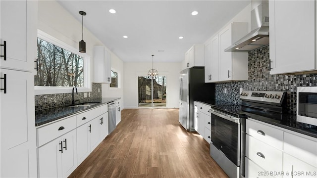 kitchen featuring decorative light fixtures, white cabinets, wall chimney range hood, and appliances with stainless steel finishes