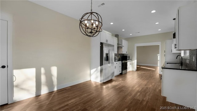 kitchen featuring stainless steel appliances, pendant lighting, wall chimney exhaust hood, white cabinets, and sink