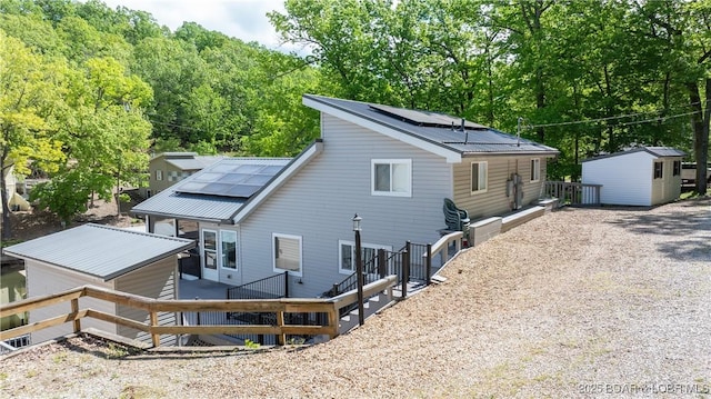 rear view of house featuring a deck, a storage shed, and solar panels