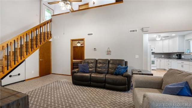 living room featuring ceiling fan, a high ceiling, and light colored carpet