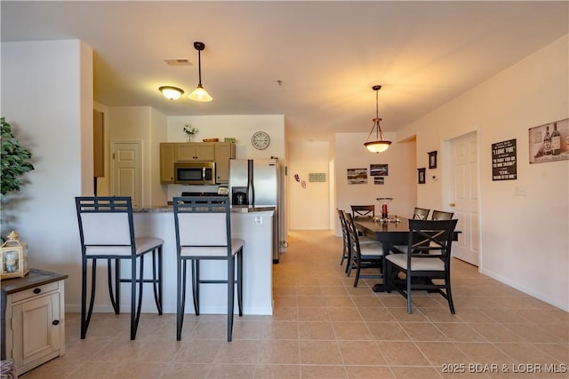 kitchen with decorative light fixtures, light tile patterned floors, appliances with stainless steel finishes, and a kitchen bar