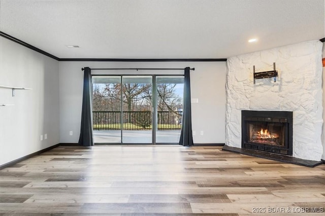 unfurnished living room with a stone fireplace, ornamental molding, and light hardwood / wood-style floors