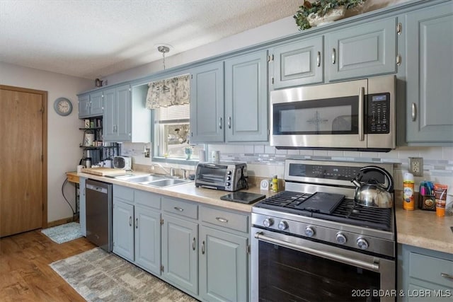 kitchen with a textured ceiling, appliances with stainless steel finishes, tasteful backsplash, sink, and hanging light fixtures