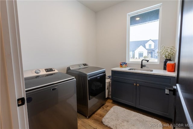 laundry room with cabinets, light hardwood / wood-style flooring, washing machine and clothes dryer, and sink