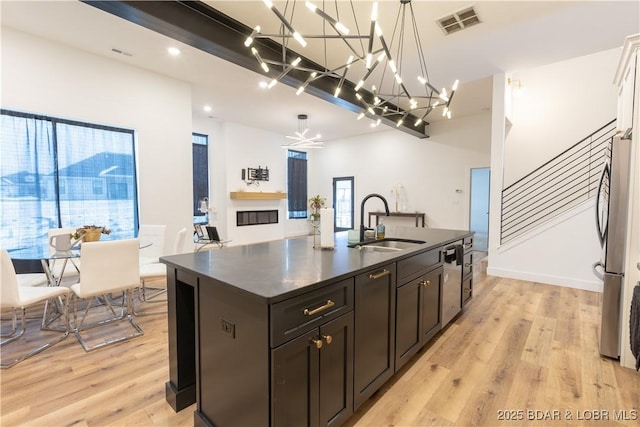 kitchen with pendant lighting, sink, light hardwood / wood-style flooring, appliances with stainless steel finishes, and an island with sink