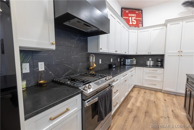 kitchen with gas range, wall chimney range hood, white cabinets, and decorative backsplash