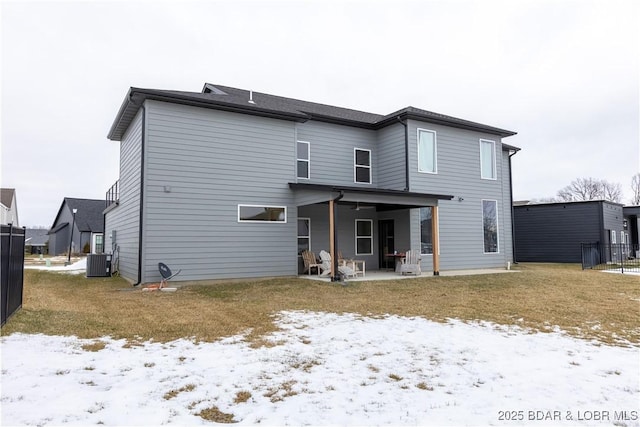 snow covered rear of property with a patio area, cooling unit, and a lawn