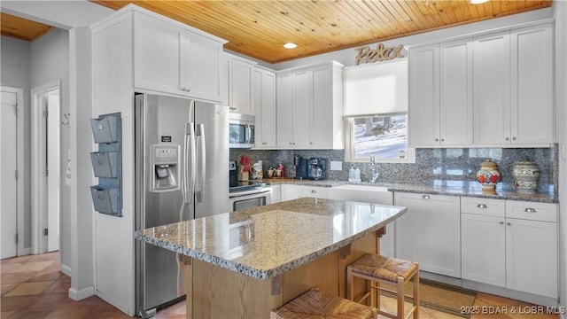 kitchen featuring stainless steel appliances, a sink, wood ceiling, a kitchen breakfast bar, and backsplash