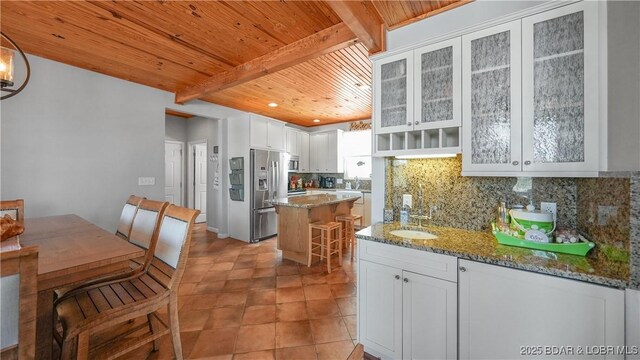 kitchen with wood ceiling, a kitchen island, tasteful backsplash, stainless steel fridge, and light stone counters