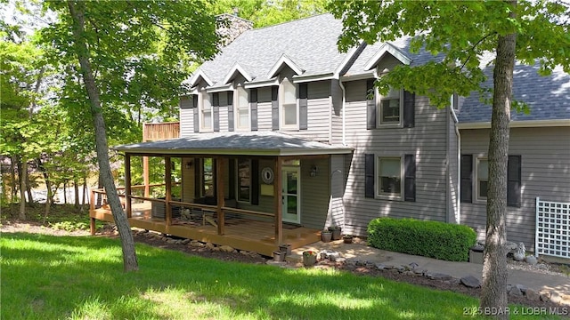 view of front of property featuring roof with shingles, a chimney, a front lawn, and a porch