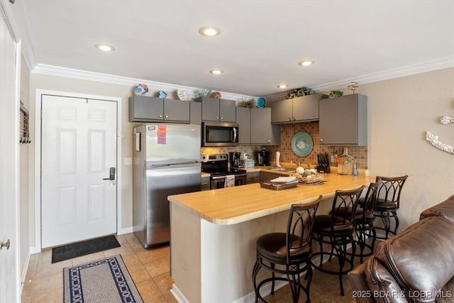 kitchen with appliances with stainless steel finishes, kitchen peninsula, light tile patterned flooring, a breakfast bar, and gray cabinetry