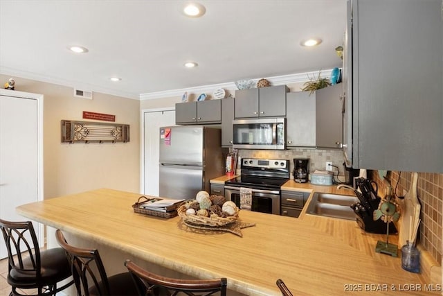 kitchen with kitchen peninsula, appliances with stainless steel finishes, decorative backsplash, crown molding, and sink