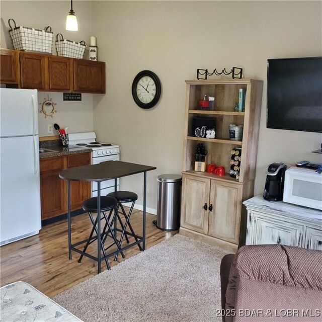 kitchen featuring dark countertops, white appliances, light wood-type flooring, and hanging light fixtures