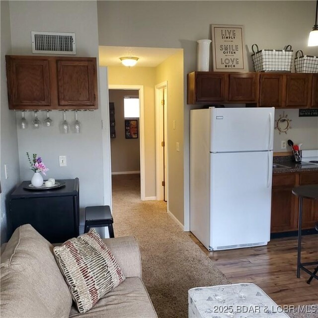 kitchen with visible vents, brown cabinetry, dark countertops, and freestanding refrigerator