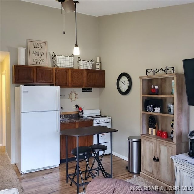 kitchen featuring white appliances, dark countertops, wood finished floors, hanging light fixtures, and a sink