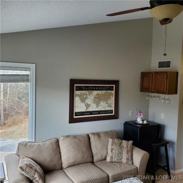 living area featuring lofted ceiling, a ceiling fan, visible vents, and a textured ceiling