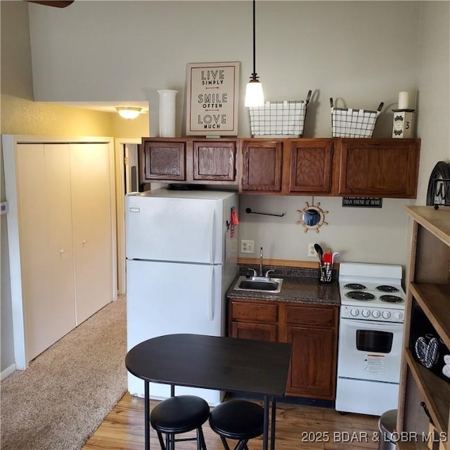 kitchen featuring white appliances, a sink, brown cabinets, dark countertops, and pendant lighting