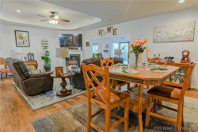 dining area with ceiling fan, a raised ceiling, and light hardwood / wood-style floors