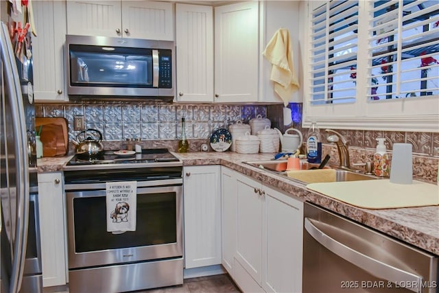 kitchen with a sink, white cabinets, light countertops, appliances with stainless steel finishes, and decorative backsplash