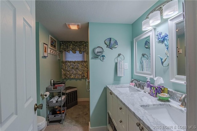 bathroom featuring a sink, toilet, double vanity, and a textured ceiling