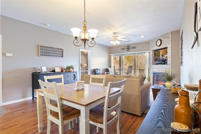 dining space with ceiling fan with notable chandelier, hardwood / wood-style floors, and a fireplace