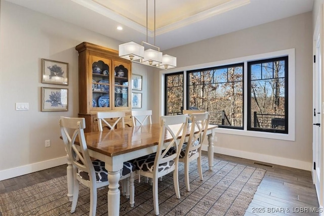 dining room with crown molding, dark wood-type flooring, an inviting chandelier, and a tray ceiling