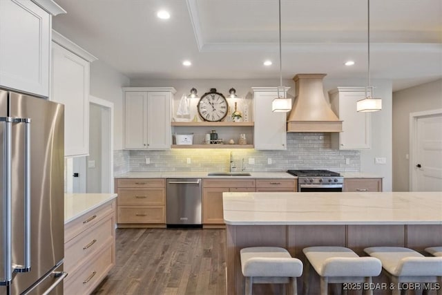 kitchen featuring sink, premium range hood, white cabinets, decorative light fixtures, and stainless steel appliances