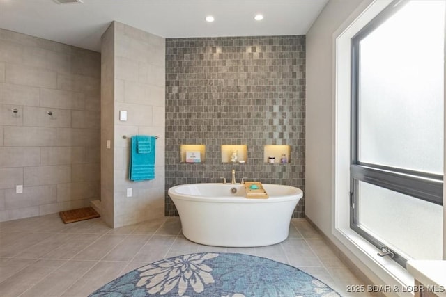 bathroom with tile patterned floors, tile walls, and a tub to relax in