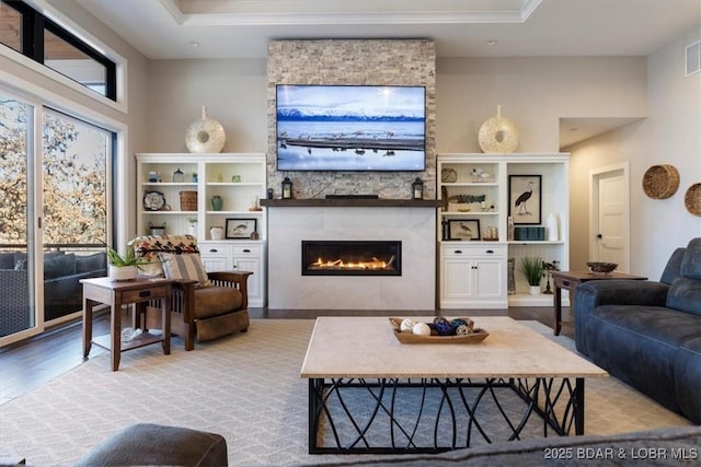 living room with a tray ceiling, a wealth of natural light, light hardwood / wood-style flooring, and a stone fireplace