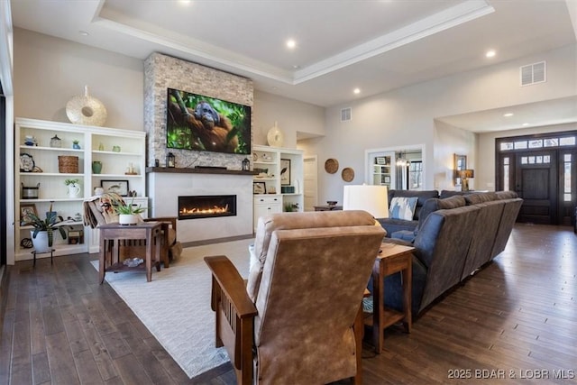 living room with a large fireplace, dark wood-type flooring, and a raised ceiling