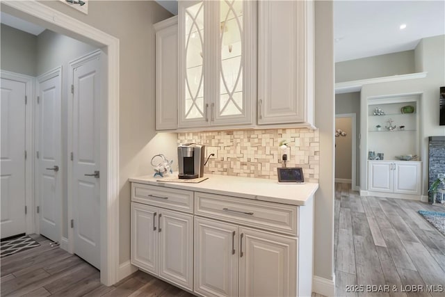 bar with light hardwood / wood-style floors, backsplash, and white cabinets