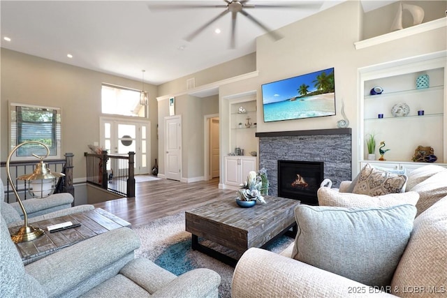 living room featuring wood-type flooring, built in shelves, and a stone fireplace