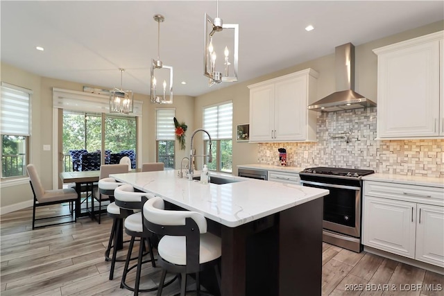 kitchen featuring stainless steel range with gas cooktop, wall chimney range hood, and white cabinets