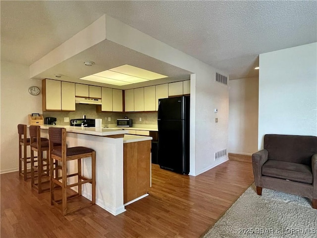 kitchen with kitchen peninsula, wood-type flooring, cream cabinetry, a textured ceiling, and black appliances