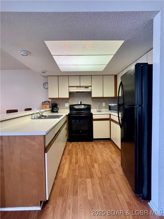 kitchen with black appliances, a textured ceiling, light wood-type flooring, sink, and kitchen peninsula