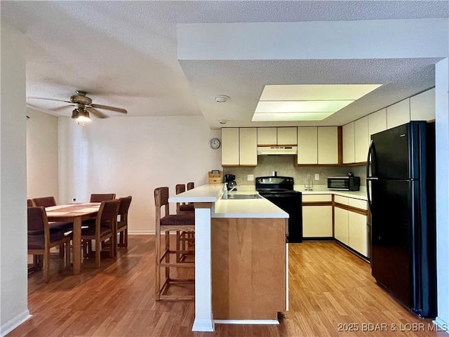 kitchen with black appliances, decorative backsplash, a kitchen breakfast bar, cream cabinetry, and kitchen peninsula